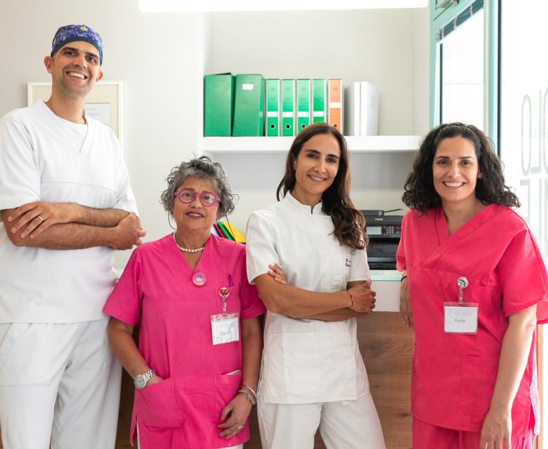 Team medico sorridente in uniforme, in una clinica con scaffali e documenti sullo sfondo.